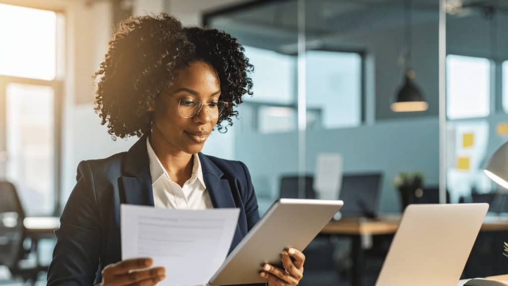 A professional woman in a suit is sitting at a desk looking at paperwork