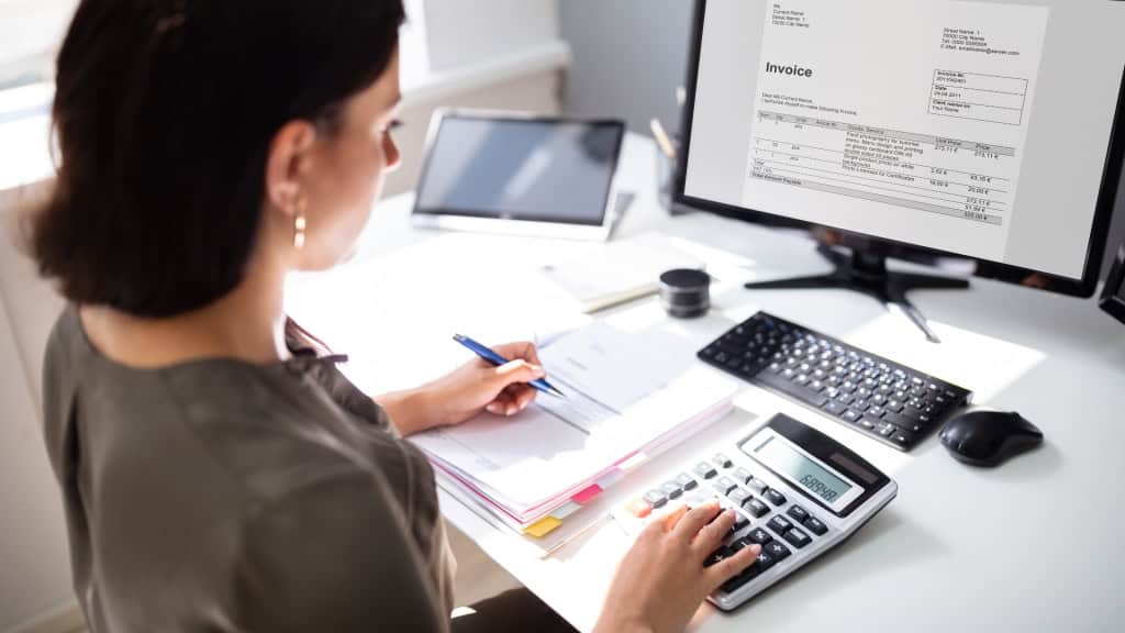 Woman working at a desk using a calculator and reviewing paperwork.