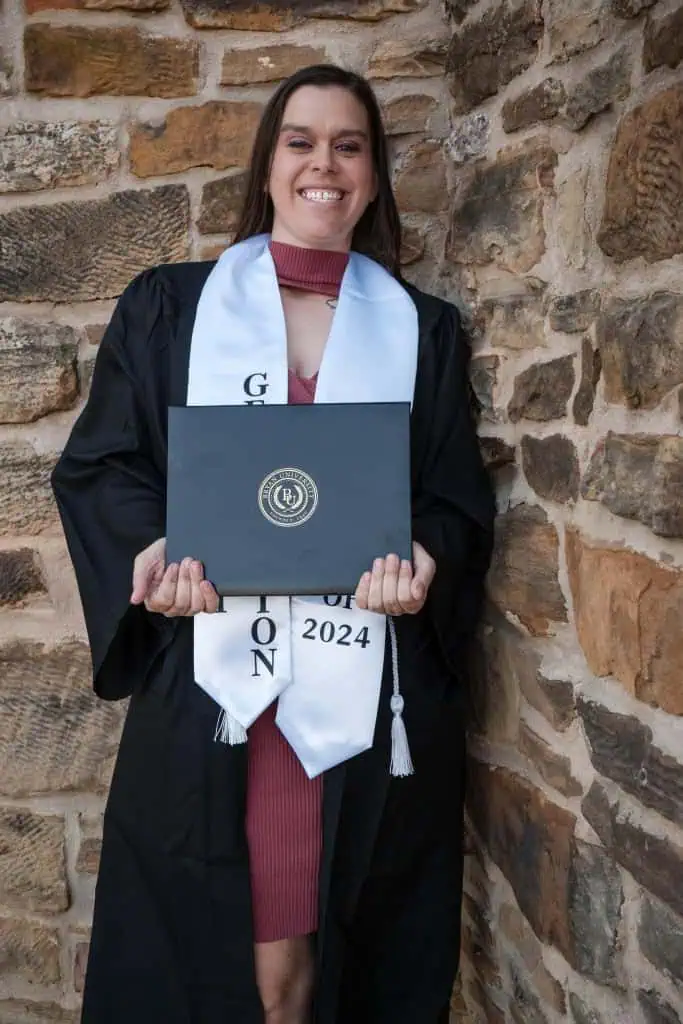 A smiling woman in a graduation gown holds a degree