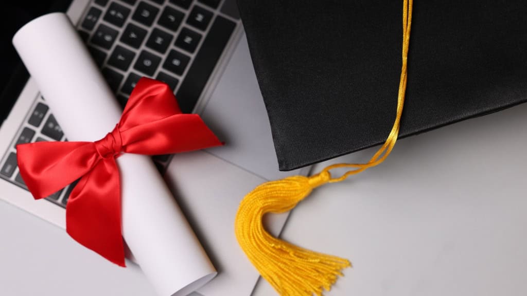 A graduation cap and diploma sit on a laptop keyboard