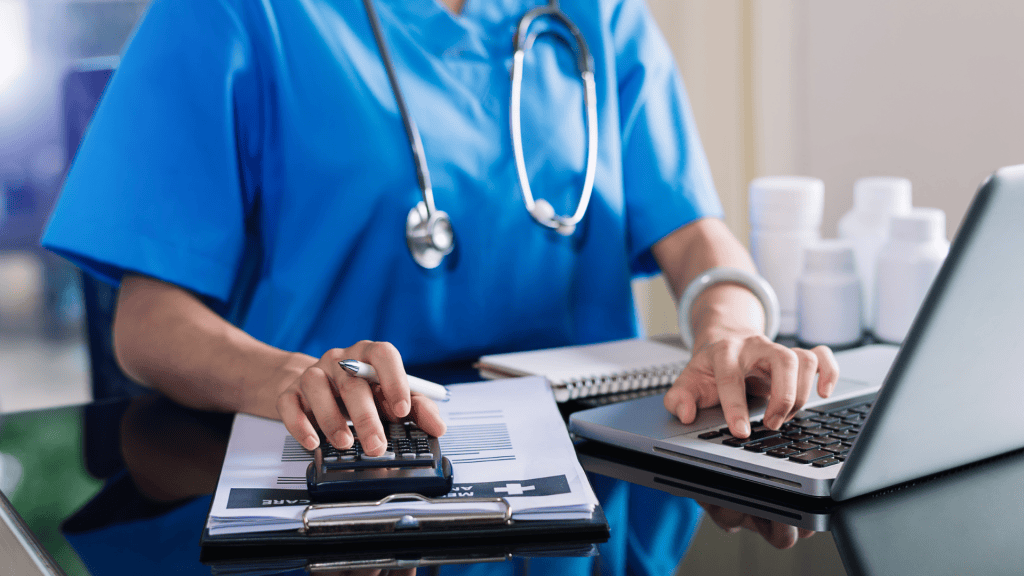 A person in scrubs sitting at a desk with a laptop