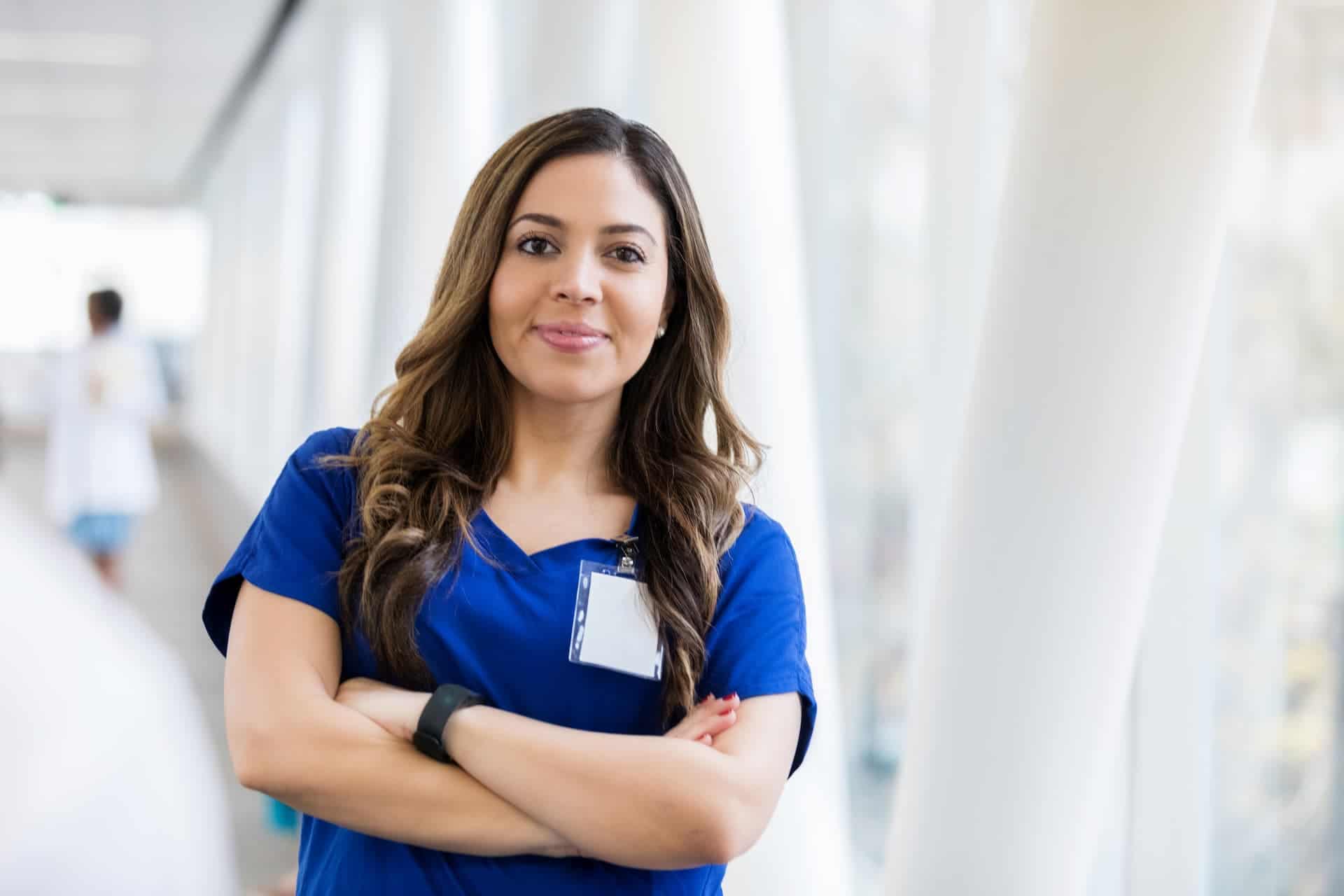 ⌙ MA Medical Assisting 6 1 Friendly female nurse in blue scrubs smiling confidently in healthcare setting.