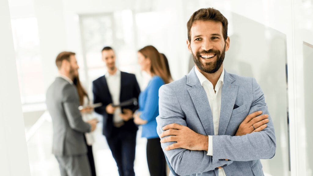 A happy man in a light blue blazer stands confidently in a modern office space