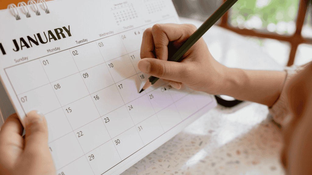 Hands holding a pen and marking a January calendar.