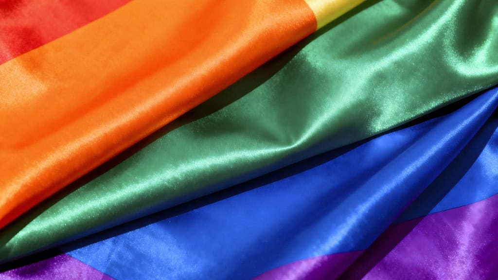 Close-up of a rainbow flag with red, orange, yellow, green, blue, and purple stripes made of shiny satin fabric.