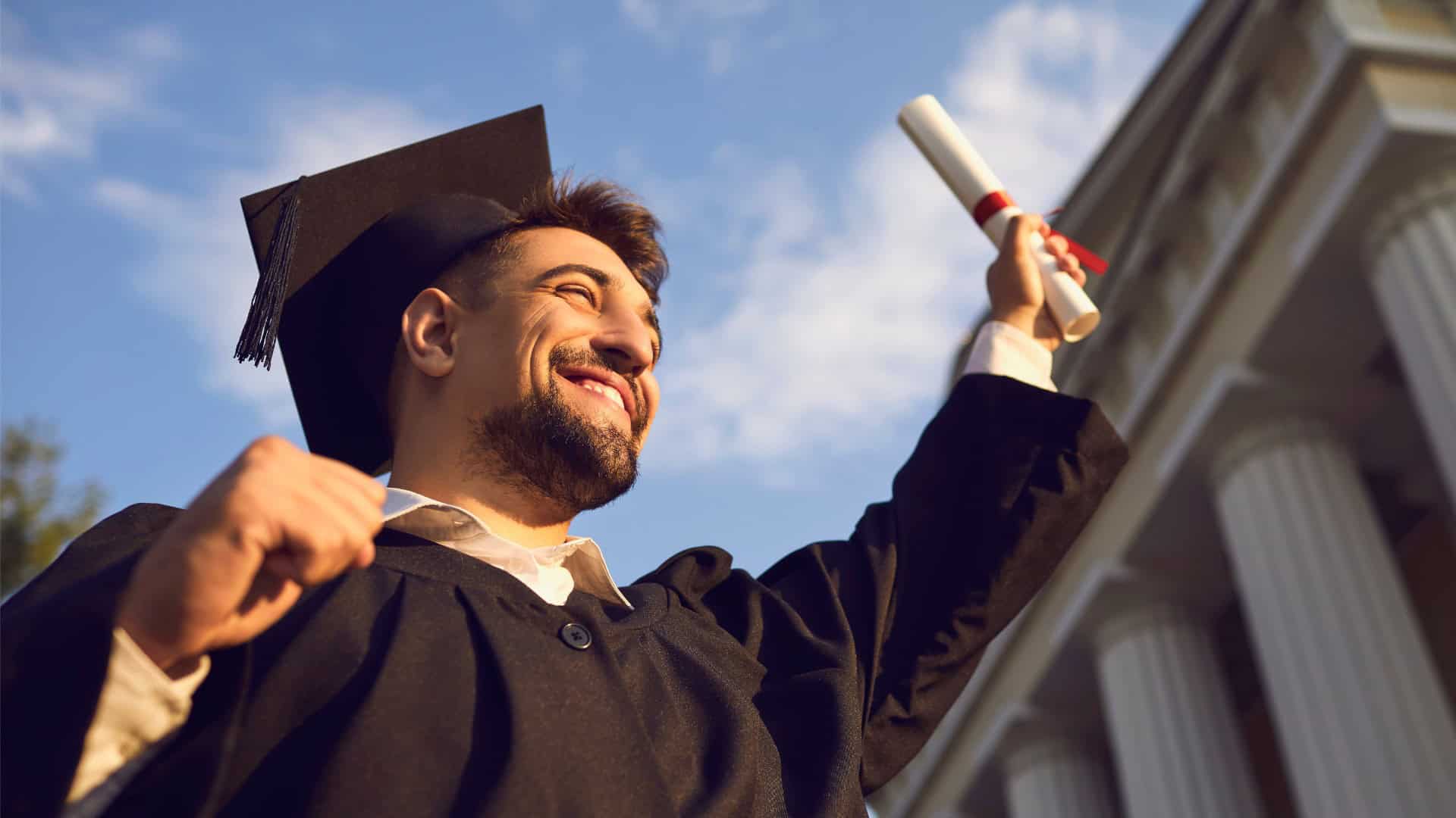A man in graduation attire smiling and holding a diploma