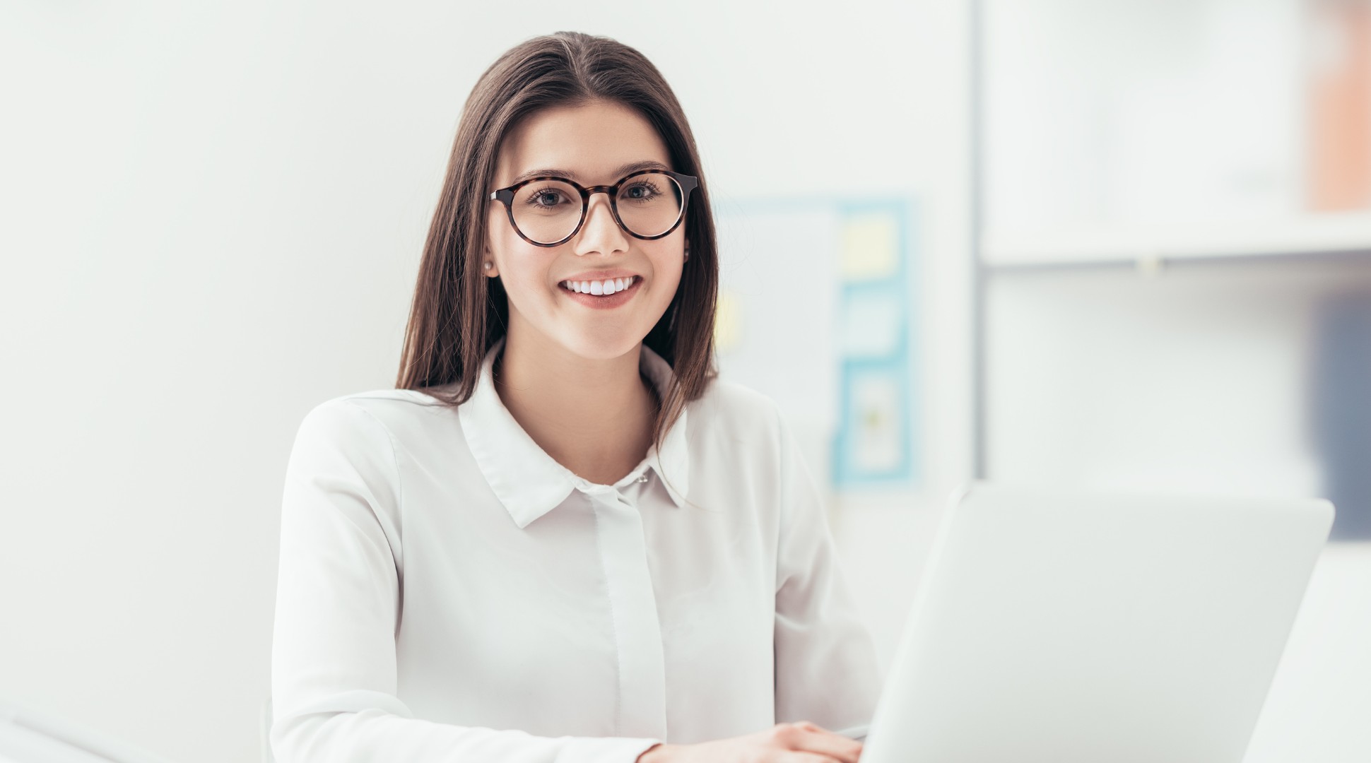 Professional woman with glasses smiling at desk in bright office setting