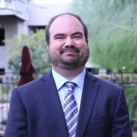 Talmage, Craig 12 A professional man in a dark business suit and patterned tie smiling at the camera outdoors.