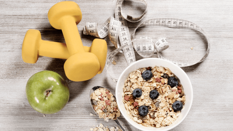 Fitness and nutrition themed flat lay with dumbbells, tape measure, apple, and oatmeal bowl with berries.