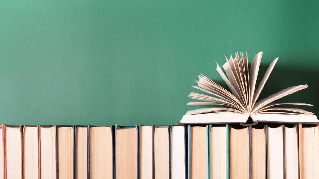 an open book on top of a stack of books in front of a green chalkboard